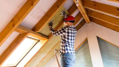 Worker installing mineral wool insulation in wall cavity
